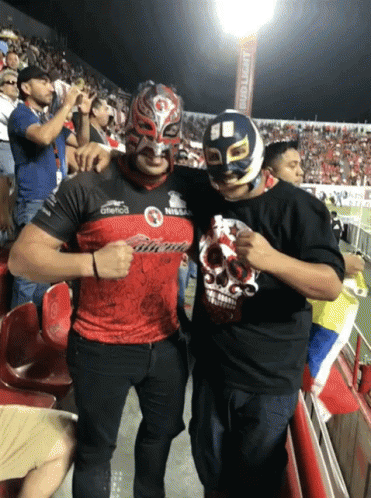 A Man Wearing A Mask Stands Next To Another Man Wearing A Shirt That Says ' Nissan ' On It GIF