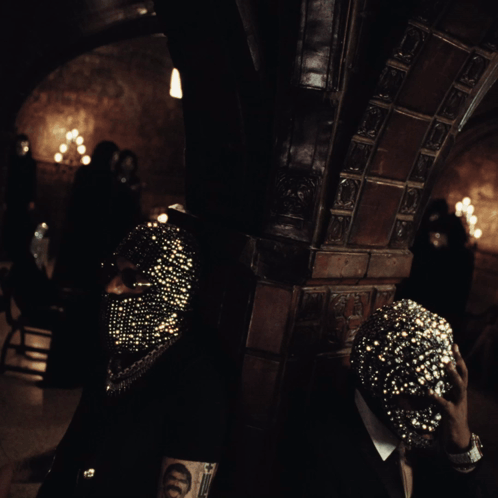 A Man Wearing A Mask With Rhinestones Is Standing In A Dark Room GIF
