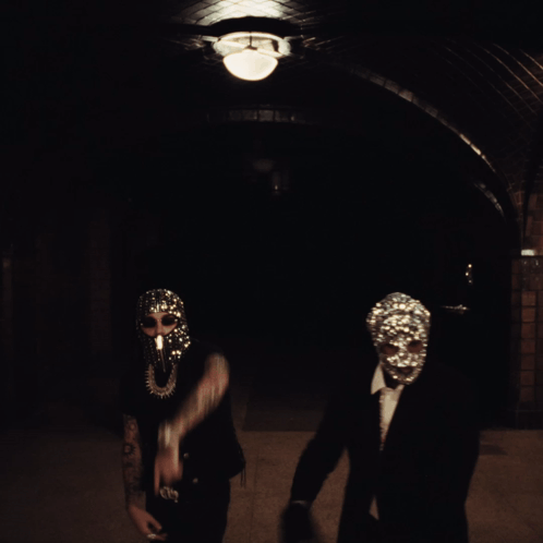 A Man Wearing A Mask With Rhinestones On It Stands Next To Another Man In A Suit GIF