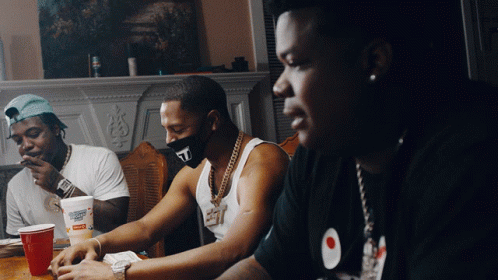 A Man Wearing A Mask With The Letter T On It Sits At A Table With Other Men GIF