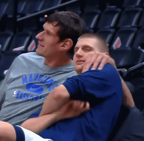 A Man Wearing A Mavericks Shirt Is Hugging Another Man In A Blue Shirt GIF