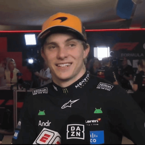 A Man Wearing A Mclaren Shirt And A Hilton Hat GIF