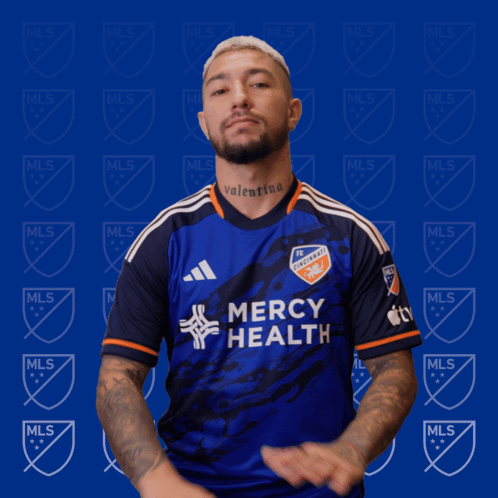 A Man Wearing A Mercy Health Jersey Stands In Front Of A Blue Background GIF