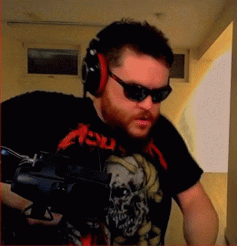 A Man Wearing A Metallica Shirt And Headphones Holds A Gun GIF