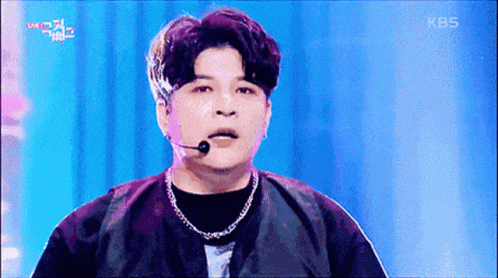 A Man Wearing A Microphone And A Necklace On A Stage With Kbs Written On The Bottom Of The Screen GIF