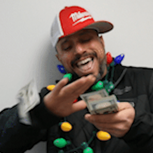 A Man Wearing A Milwaukee Hat Is Holding A String Of Christmas Lights Around His Neck GIF