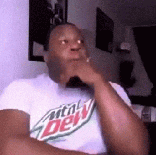 a man wearing a mountain dew t-shirt is sitting in a chair with his hand on his chin .
