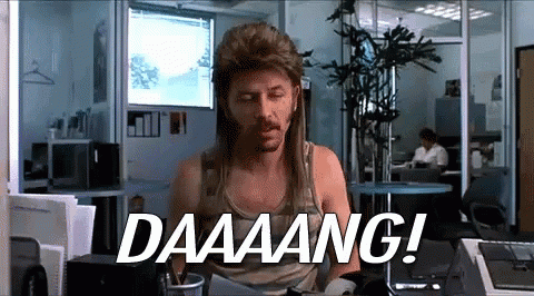A Man Wearing A Mullet Is Sitting At A Desk And Says Daaaang ! GIF