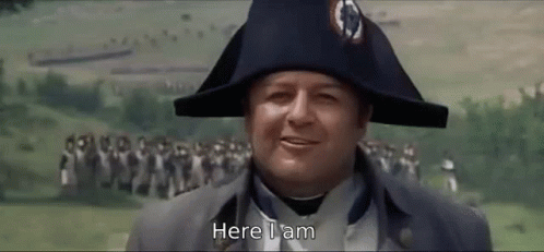 A Man Wearing A Napoleon Hat Is Standing In Front Of A Crowd And Says Here I Am . GIF