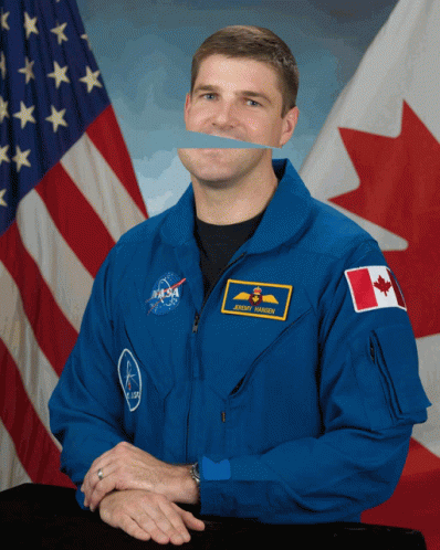 A Man Wearing A Nasa Uniform Stands In Front Of A Canadian And American Flag GIF