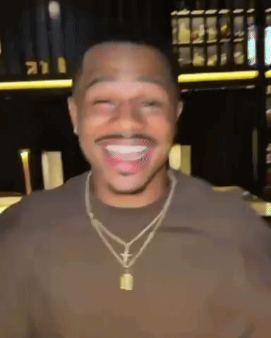 a man wearing a necklace and a brown shirt is smiling and making a funny face .