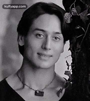 A Man Wearing A Necklace Is Smiling In A Black And White Photo . GIF