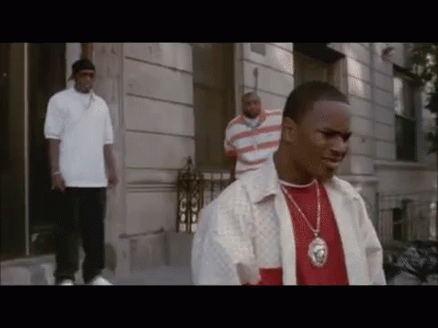 A Man Wearing A Necklace With A Lion On It Is Standing In Front Of A Building GIF