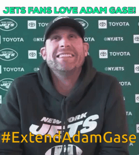 A Man Wearing A New York Jets Hoodie Smiles In Front Of A Green Backdrop GIF