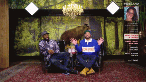 A Man Wearing A New York Shirt Sits Next To Another Man On A Couch GIF
