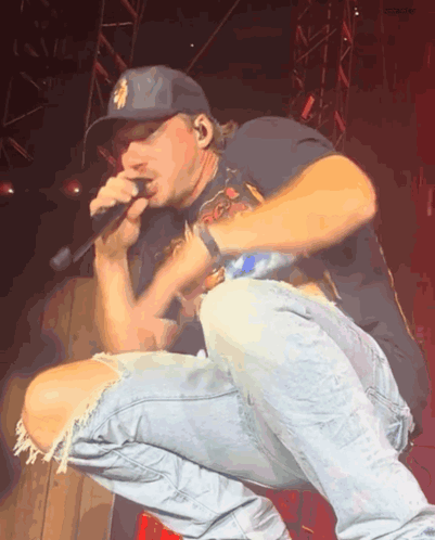 A Man Wearing A New York Yankees Hat Is Singing Into A Microphone On A Stage GIF
