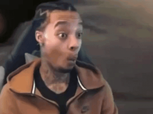 a man wearing a nike jacket is making a surprised face while sitting in a chair .