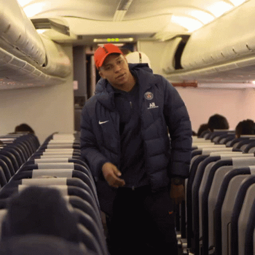 A Man Wearing A Nike Jacket Stands In An Airplane Aisle GIF