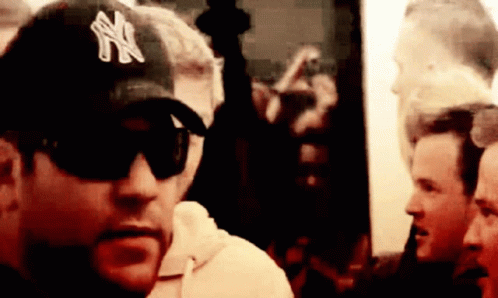 A Man Wearing A Ny Hat And Sunglasses Looks At The Camera GIF