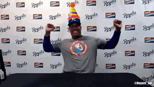 A Man Wearing A Party Hat Is Standing In Front Of A Wall That Says Royals On It GIF