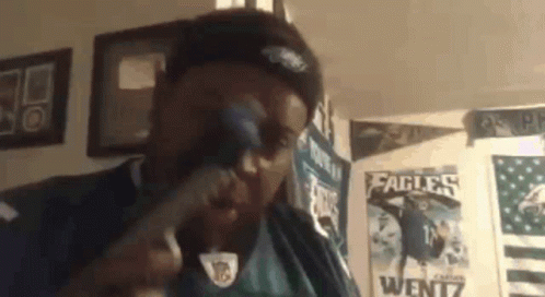 A Man Wearing A Philadelphia Eagles Jersey Is Singing Into A Microphone In A Room . GIF