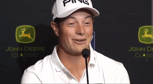a man wearing a ping hat stands in front of a john deere logo