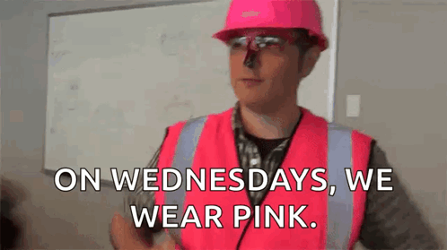 A Man Wearing A Pink Hard Hat And Safety Vest Is Standing In Front Of A Whiteboard . GIF