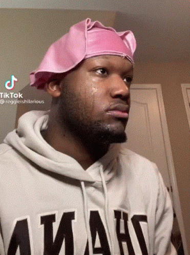 A Man Wearing A Pink Hat And A Hoodie That Says ' Amans ' GIF