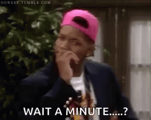 A Man Wearing A Pink Hat And A Suit Is Holding His Hand To His Chin And Says Wait A Minute . GIF