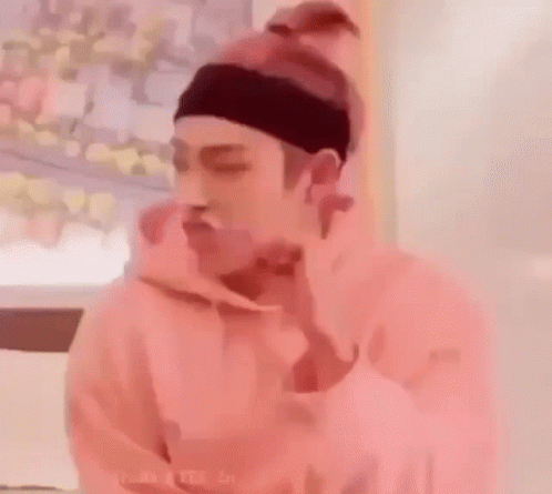 A Man Wearing A Pink Hoodie And A Headband Is Eating A Sandwich . GIF