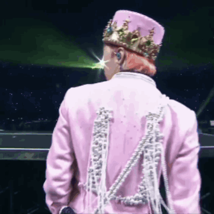 A Man Wearing A Pink Jacket And A Crown Is Standing On A Stage . GIF