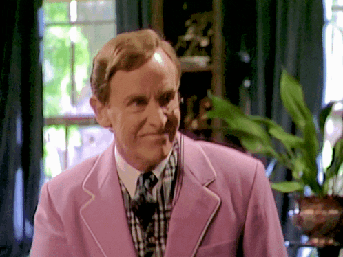A Man Wearing A Pink Jacket And Tie Smiles GIF