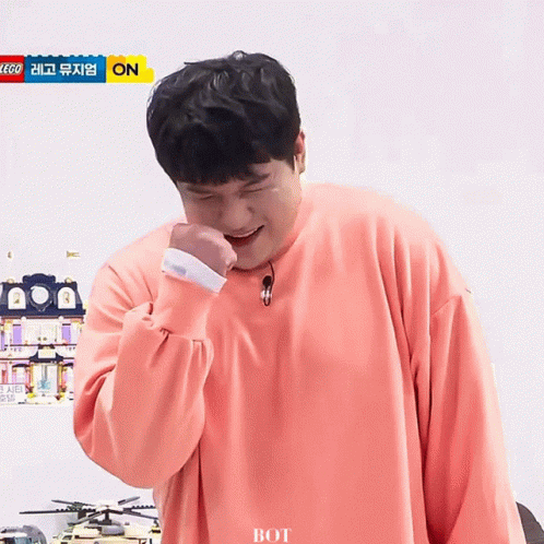 a man wearing a pink sweater is laughing in front of a sign that says lego on it