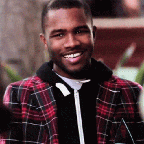A Man Wearing A Plaid Jacket Is Smiling And Looking At The Camera GIF