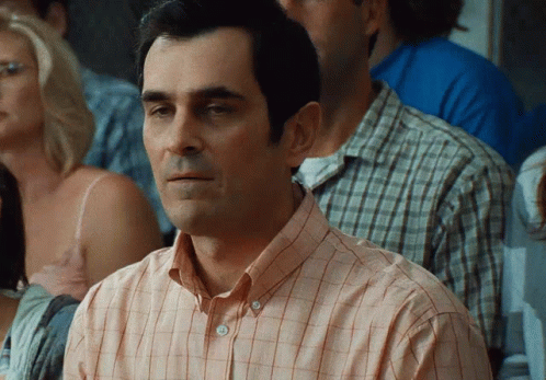 A Man Wearing A Plaid Shirt Is Sitting In A Crowd GIF