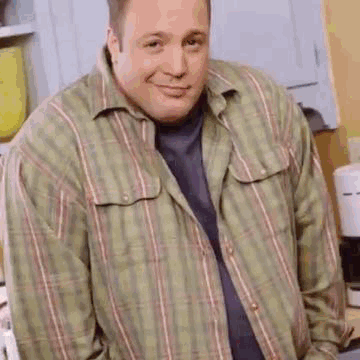 A Man Wearing A Plaid Shirt Is Standing In A Kitchen . GIF