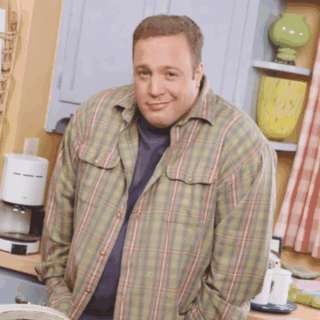 A Man Wearing A Plaid Shirt Is Standing In A Kitchen With His Hands In His Pockets GIF
