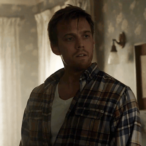 A Man Wearing A Plaid Shirt Is Standing In A Room GIF