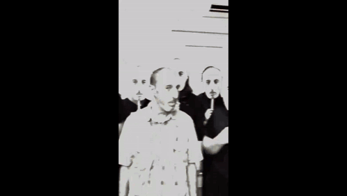 A Man Wearing A Plaid Shirt Is Surrounded By Other Men With Red Faces On Sticks GIF