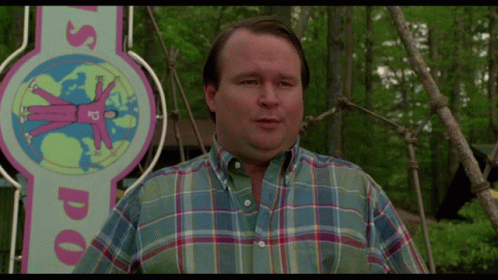 A Man Wearing A Plaid Shirt Stands In Front Of A Sign That Says Us Doo GIF