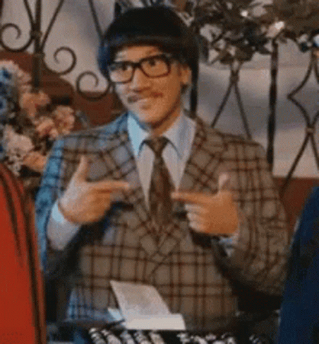 A Man Wearing A Plaid Suit And Tie Is Pointing At Something . GIF