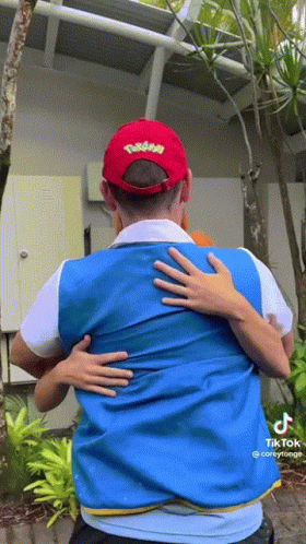 a man wearing a pokemon hat is hugging another man wearing a blue vest