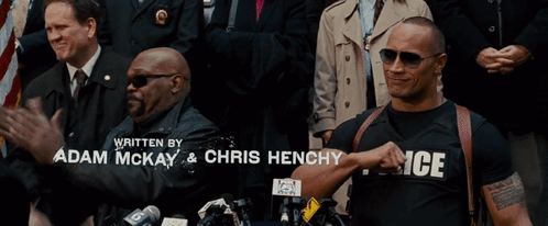 A Man Wearing A Police Shirt Is Standing In Front Of A Crowd Of People GIF