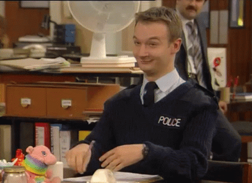A Man Wearing A Police Sweater Sits At A Desk GIF