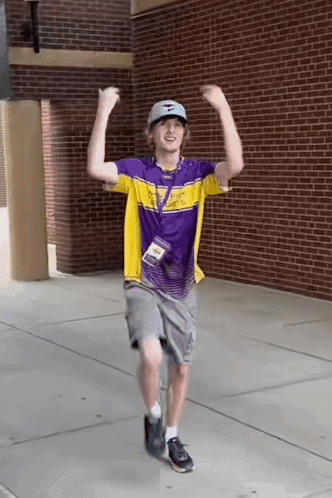 A Man Wearing A Purple And Yellow Shirt Is Dancing On The Sidewalk . GIF