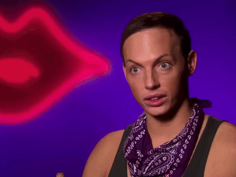 A Man Wearing A Purple Bandana Is Sitting In Front Of A Neon Lip GIF