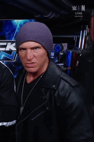 A Man Wearing A Purple Hat Is Making A Funny Face In Front Of A Wrestling Logo GIF