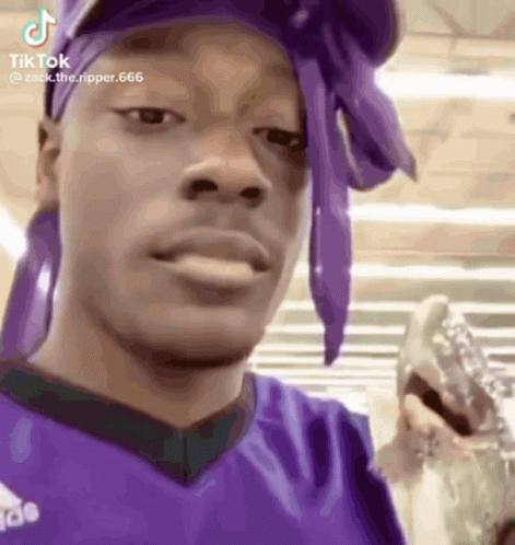 A Man Wearing A Purple Headband And A Purple Shirt Is Holding A Glass Of Water . GIF