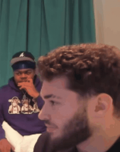 A Man Wearing A Purple Hoodie Is Sitting Next To Another Man GIF