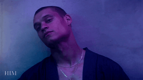 A Man Wearing A Purple Shirt And A Necklace With The Word Him Below Him GIF